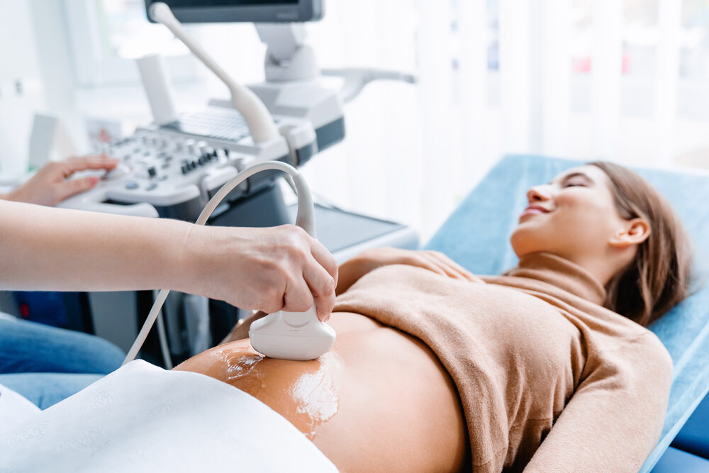 A healthcare professional performs an abdominal ultrasound on a pregnant woman lying on an examination table.