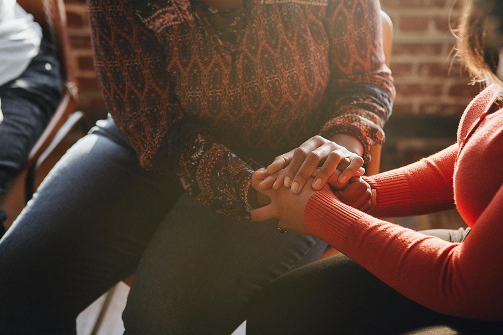Close-up of two people sitting together and holding hands in a supportive gesture.