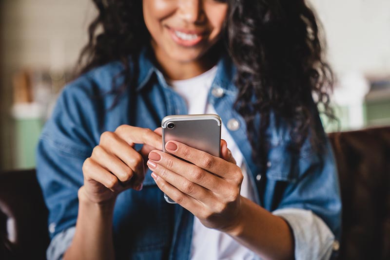Young african-american woman smiling as she looks at the screen on her cell phone.