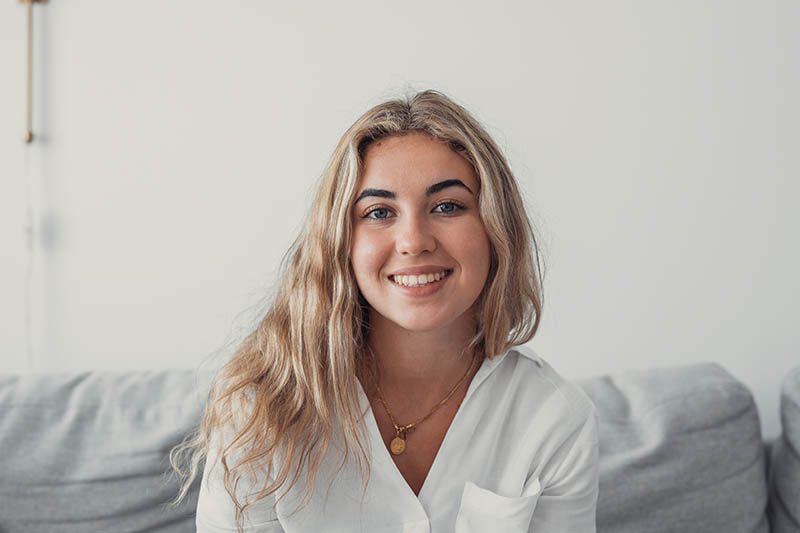 Happy young woman with blonde hair smiling at the camera in a well lit room.