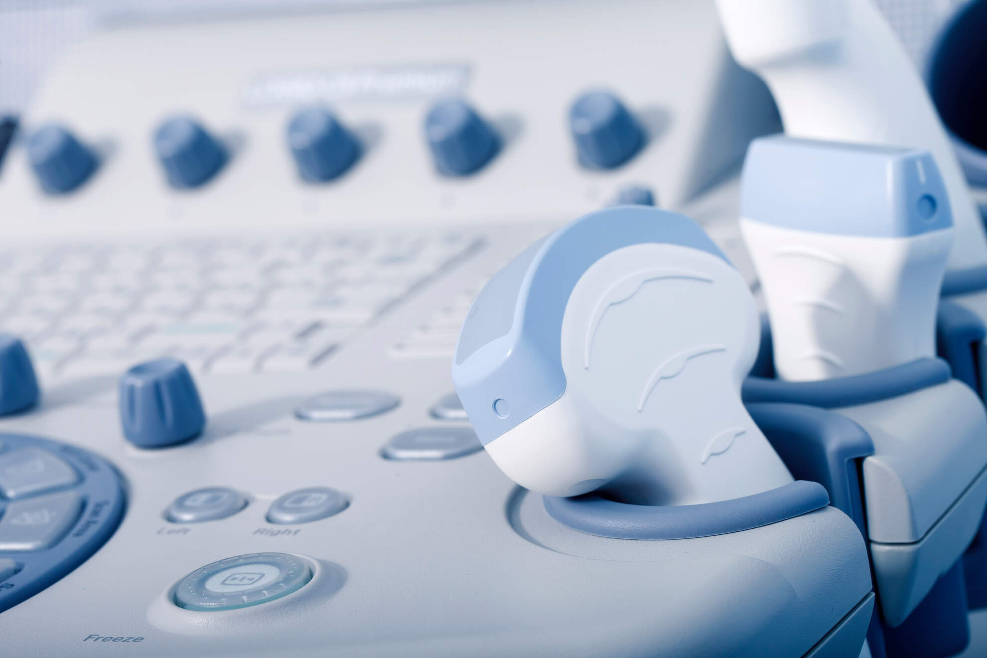 Close-up of a modern ultrasound machine control panel with various buttons, dials, and a handheld transducer probe.